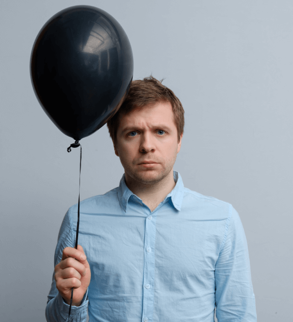 sad looking man holds a black balloon (a metaphor for his car loan with a big balloon payment).
